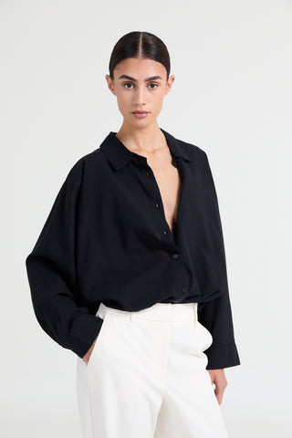 Woman wearing a black blouse with a deep neckline and white pants on a white background