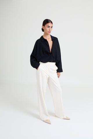Woman wearing a black blouse and white pants on a white background