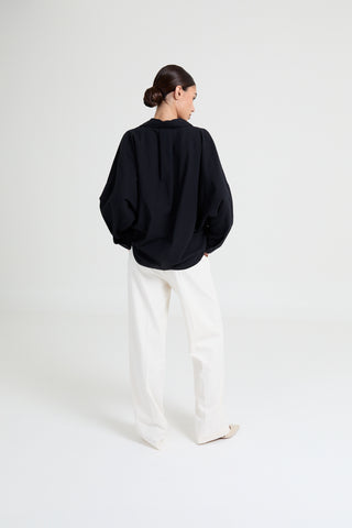 Person wearing a black oversized sweater and white pants on a white background
