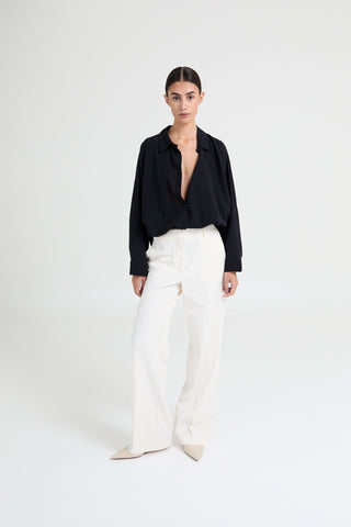 Person wearing a black blouse and white pants on a white background