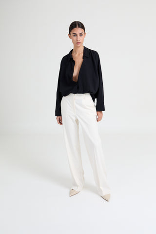 Person wearing a black blouse and white pants on a white background