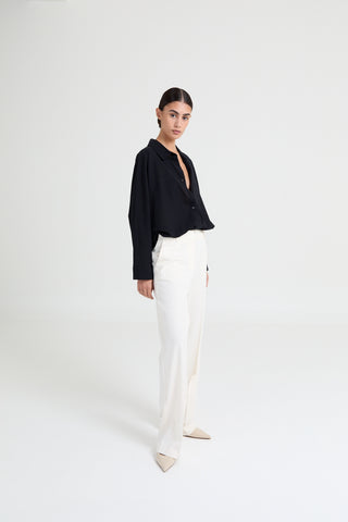 Woman wearing a black blouse and white pants on a white background