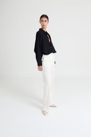 Person wearing a black top and white pants on a white background