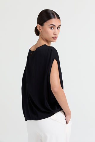 Woman wearing a black top and white pants on a light gray background