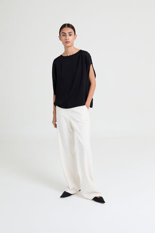 Person wearing a black top and white pants on a white background