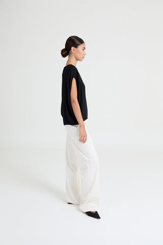 Woman wearing a black top and white pants on a white background