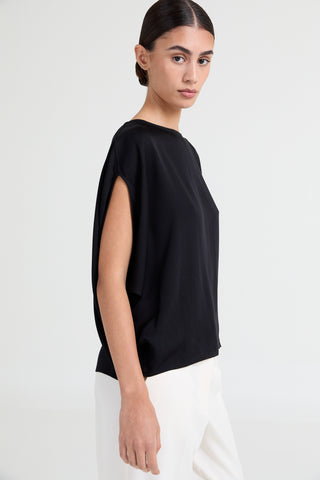 Woman wearing a black top and white pants on a plain background