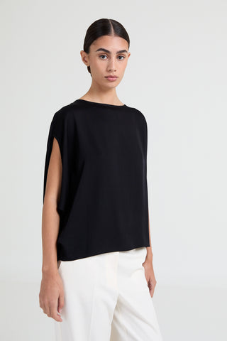 Woman wearing a black top and white pants on a plain background