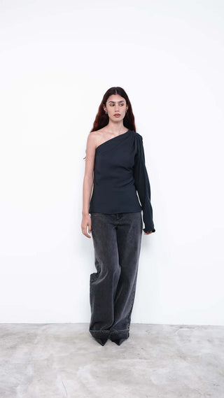 Model wearing black one-shoulder top with wide-leg jeans
