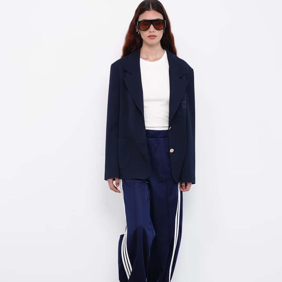 Model wearing navy blazer with satin track pants and white top